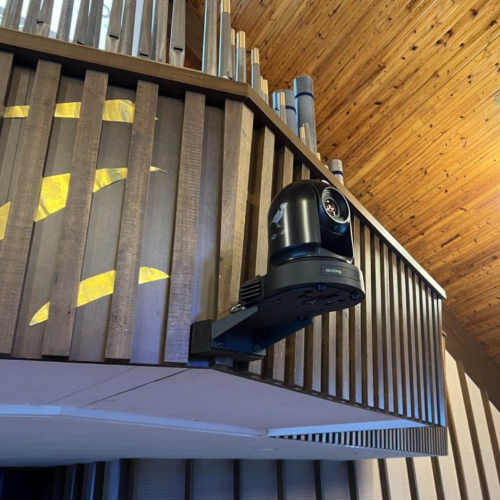 A Bird Dog live stream camera mounted at the back of the sanctuary of a church.