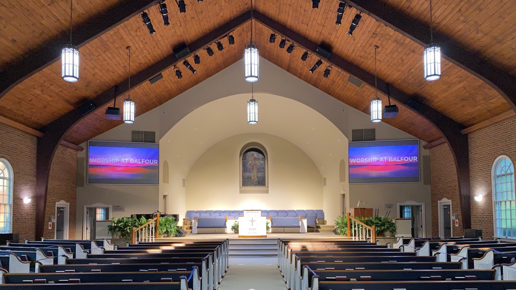 An empty church sanctuary with two large screens and projectors and numerous lights and speakers for a complete AV package.