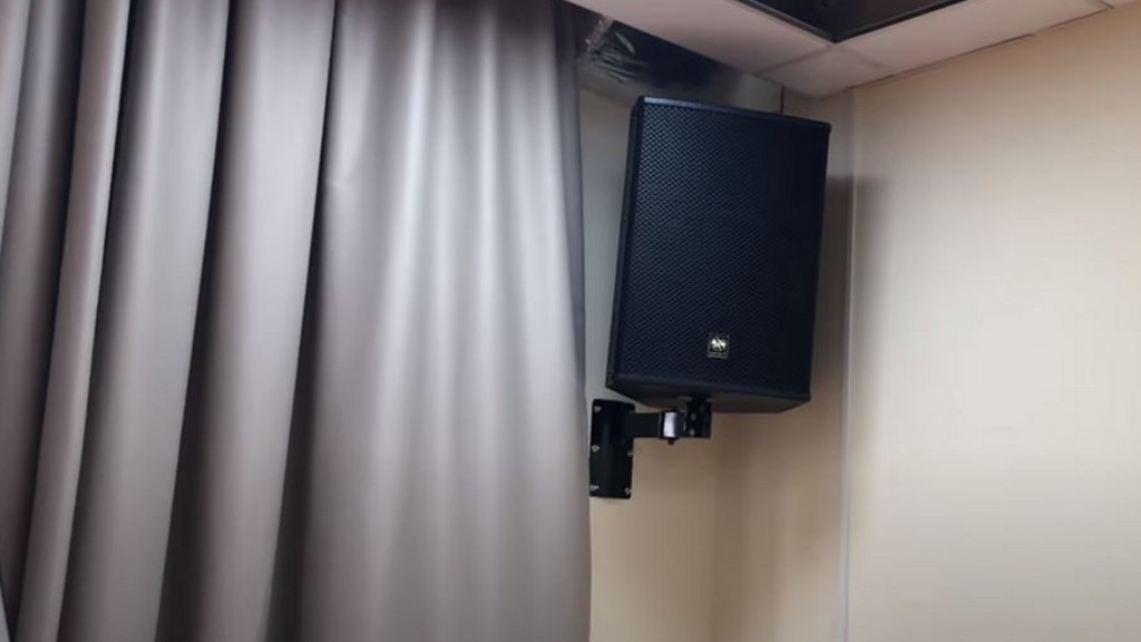 A wall-mounted speaker in the corner of a conference room, hanging next to a copper-colored curtain.