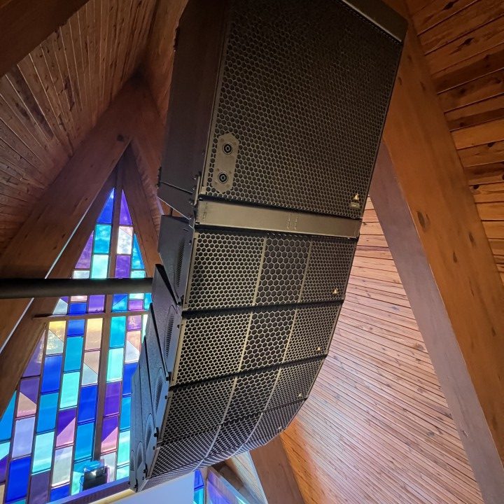 An Adamson line array speaker hanging from the ceiling of a church sanctuary.