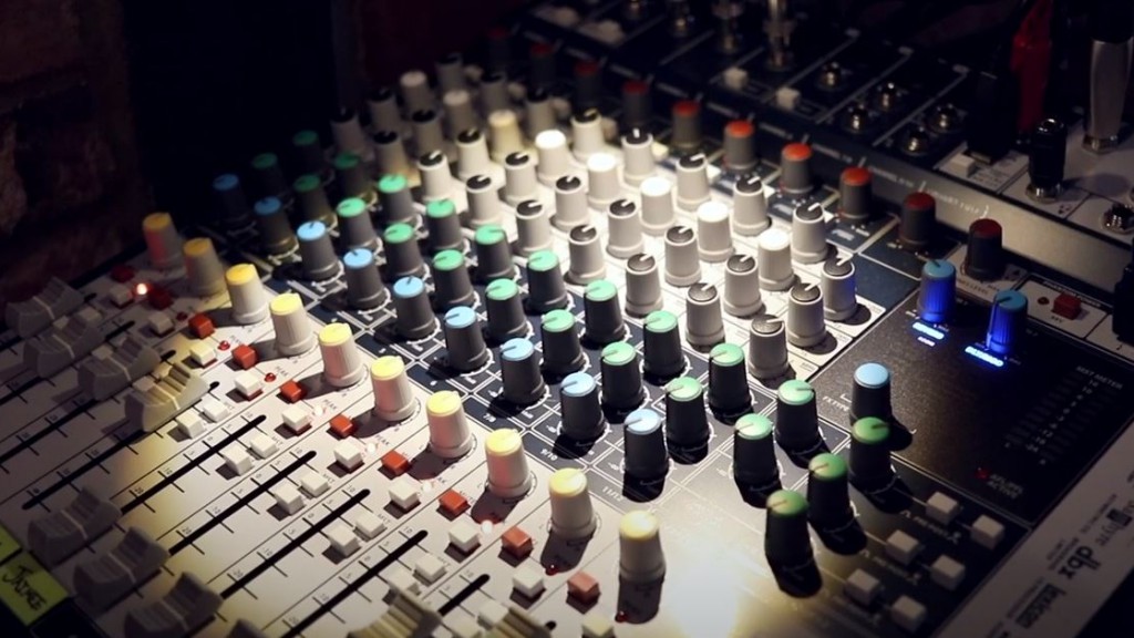 Close-up photo of dozens of colorful knobs on a sound mixing board under a tiny spotlight to help the sound engineer see in a dark church.