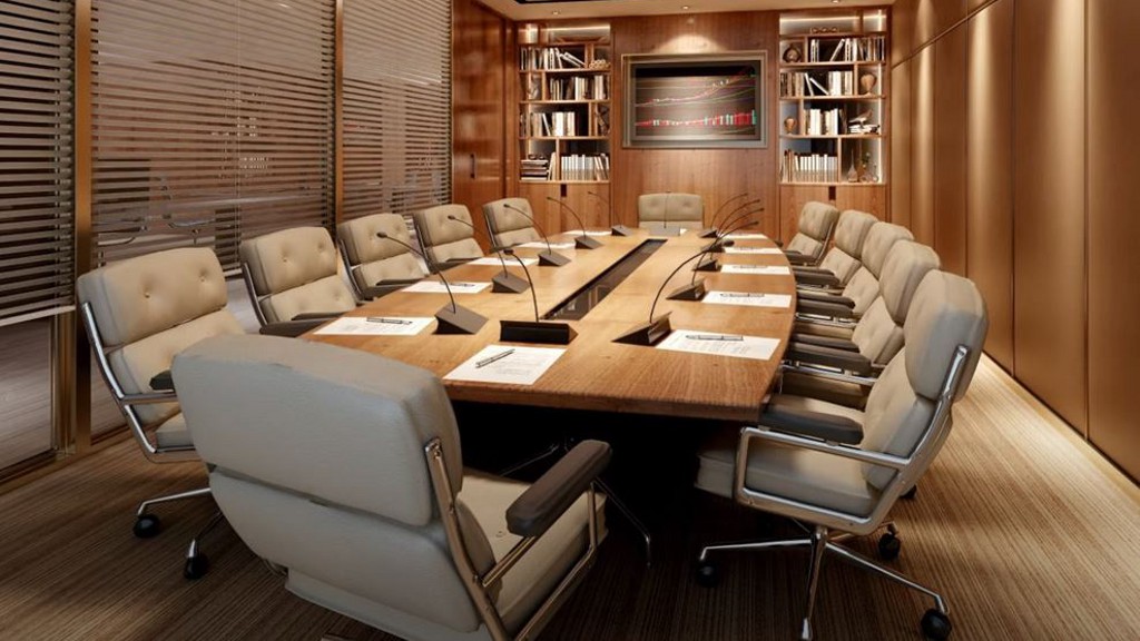 An elegant, modern conference room with 12 padded chairs around a sleek wooden table. Each seat has its own microphone for clear audio on conference calls. A video screen hangs on the wall at one end of the table, flanked by decorative bookcases.