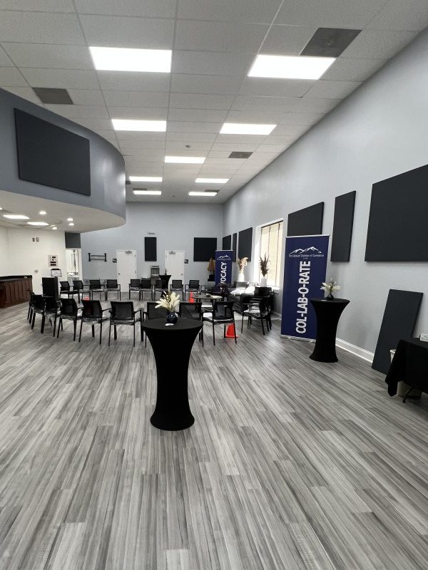 A renovated gathering space with sleek grey-white laminate floor, black chairs, and bar tables. Modern black acoustic panels hang on the walls.