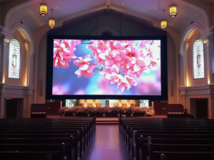 A large LED video wall displays vibrant pink flowers and casts a soft light on the inside of a church sanctuary.