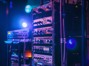 A rack of professional audiovisual equipment, including audio mixers and signal processors, illuminated by stage lights in a dimly lit environment. What is AV equipment?