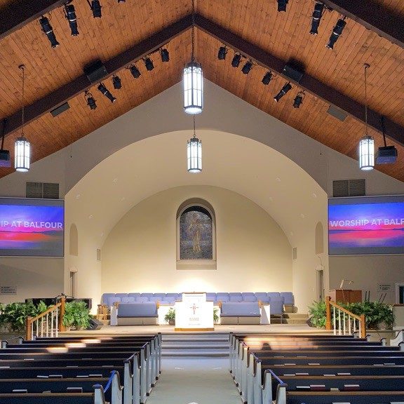 An empty church sanctuary with two large screens and projectors and numerous lights and speakers for a complete AV package.